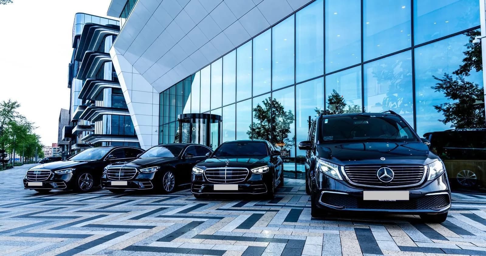 Schipholride VIP-vloot: Mercedes S-Class en V-Class voor een modern glazen gebouw in de avondschemering