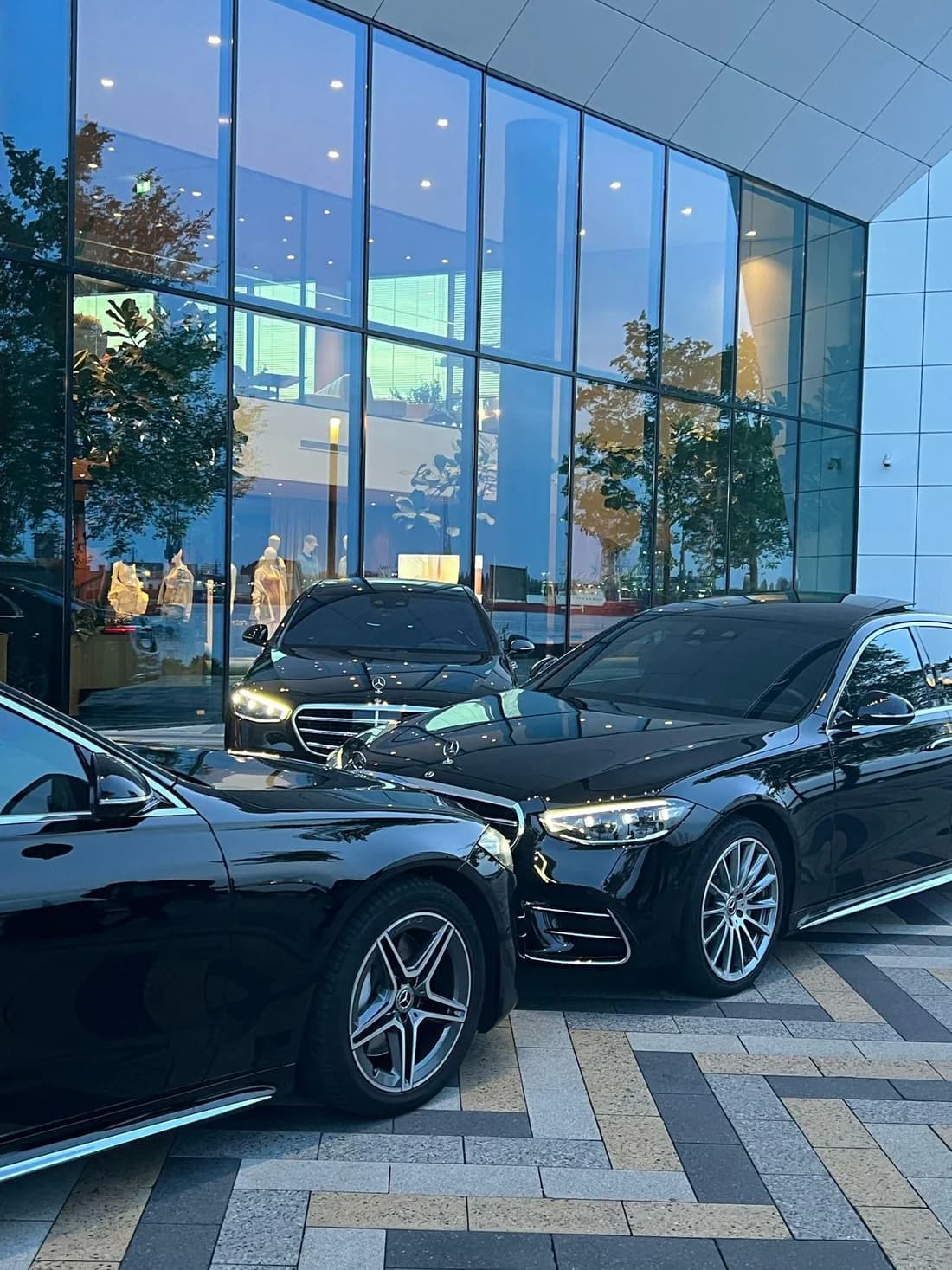 Twee zwarte Mercedes S-Class voor een verlichte glazen gevel bij avond