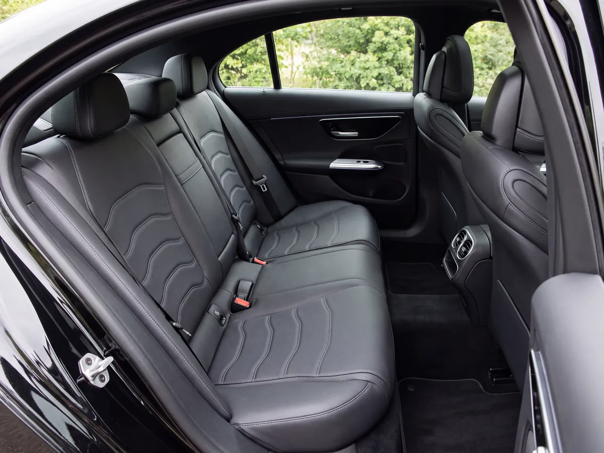 Back seat of a car with grey leather upholstery and visible seat belts, in daylight