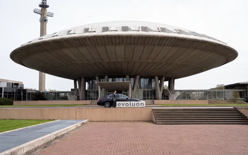 Het Evoluon in Eindhoven, met ervoor een zwarte sedan en een chauffeur in pak
