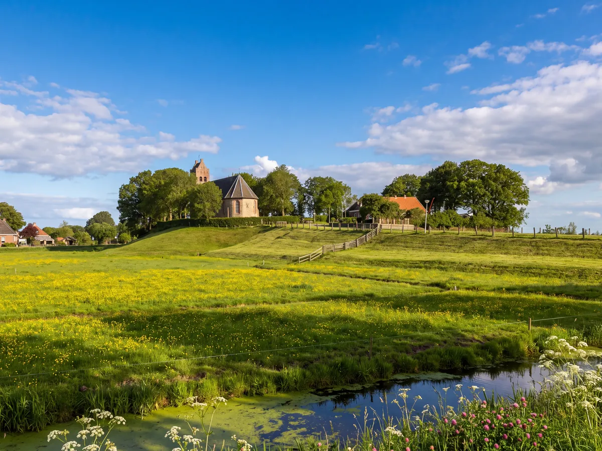 Village church on a mound above meadows of buttercups and a ditch