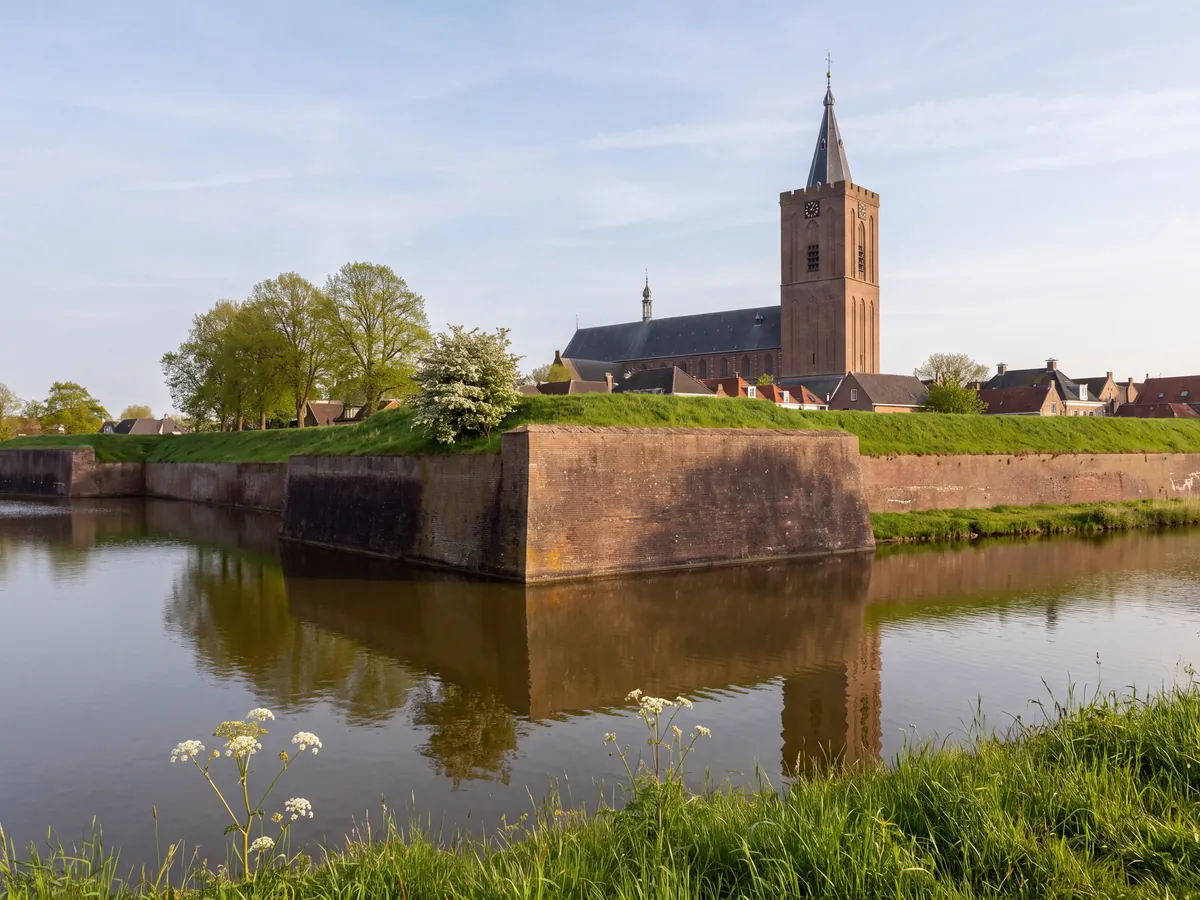 Fortress wall by the water with a church tower in 't Gooi