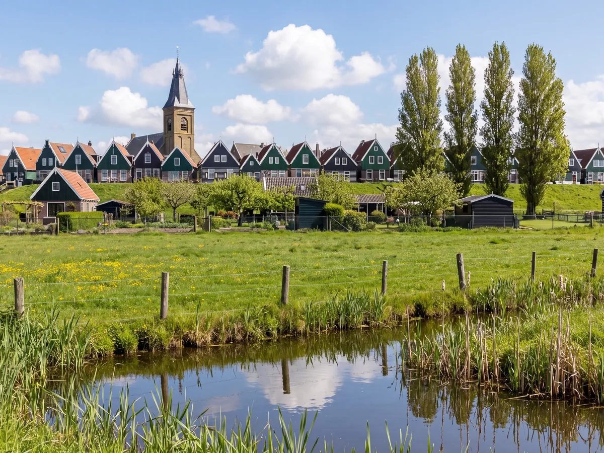 Green wooden houses and a church tower beyond a meadow and ditch in Waterland