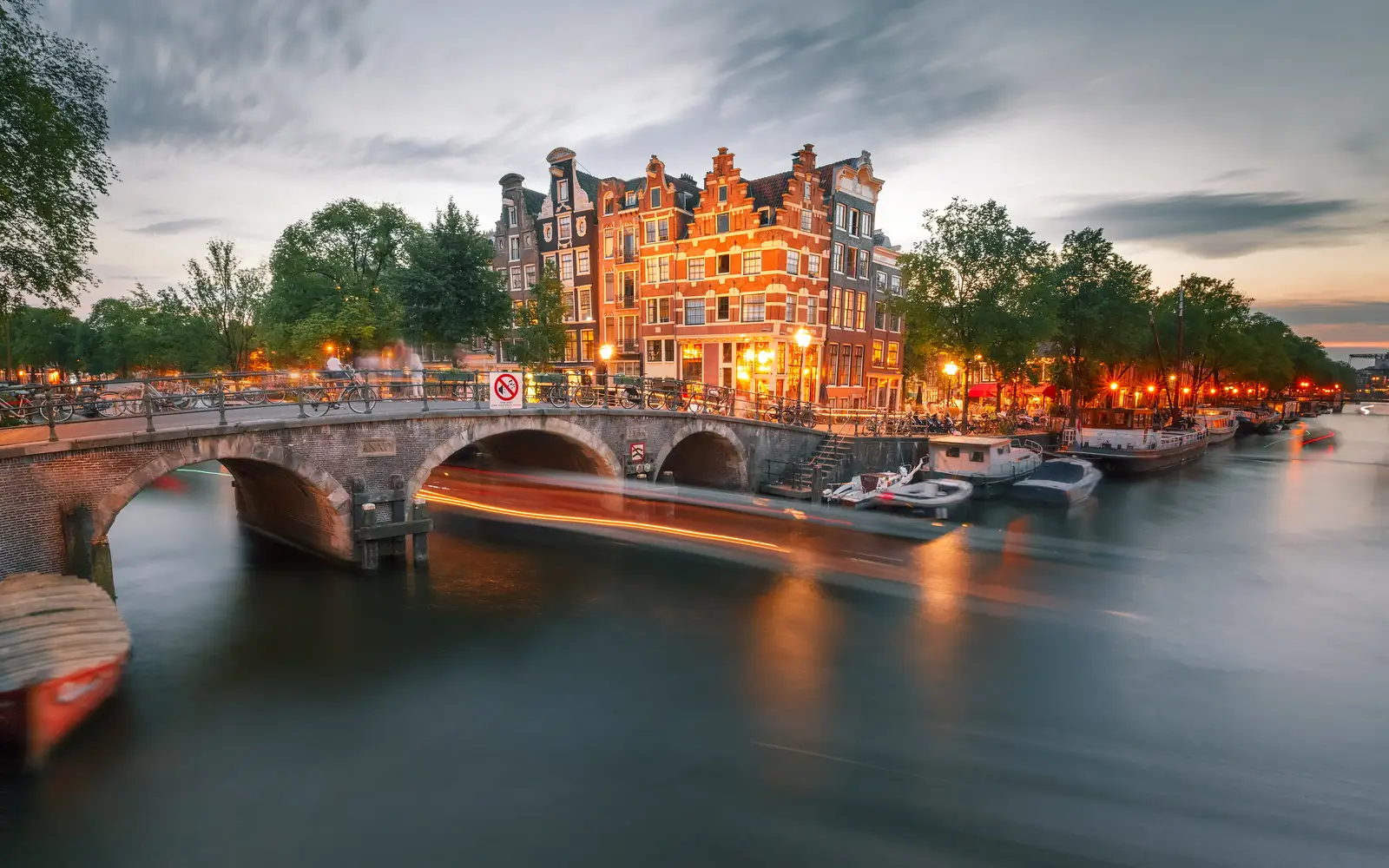 Amsterdam canal with a stone bridge and lit canal houses in the evening
