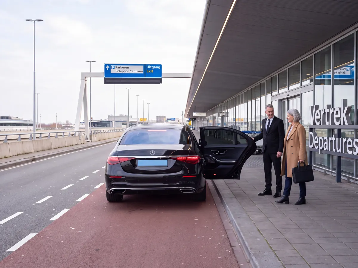Driver holding the rear door of a black sedan open at the Schiphol departures drop-off