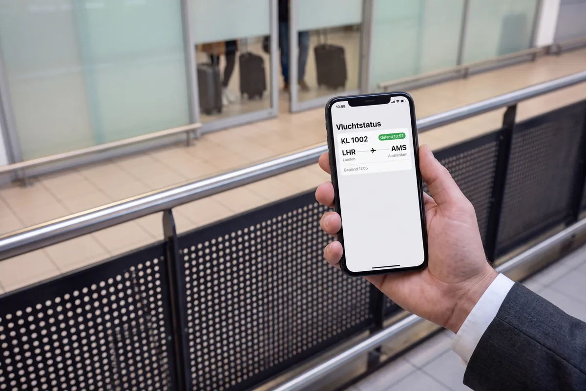 Hand holding a phone showing a flight status, with the arrivals hall blurred in the background